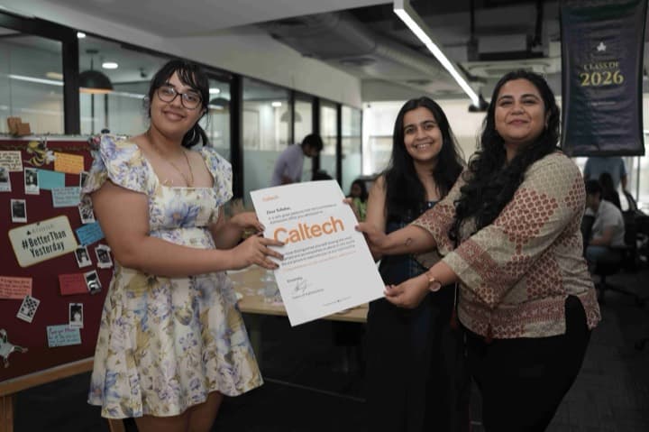 A student holds up her Caltech admission letter with two others celebrating beside her